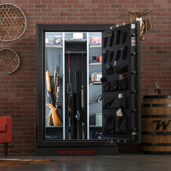 The open Winchester Safe Big Daddy XLT2 gun safe, featuring the advanced GunStiXX storage system and an impressive fire rating, neatly organizes rifles, shotguns, fishing rods, and gear on shelves and door pockets against a brick wall.